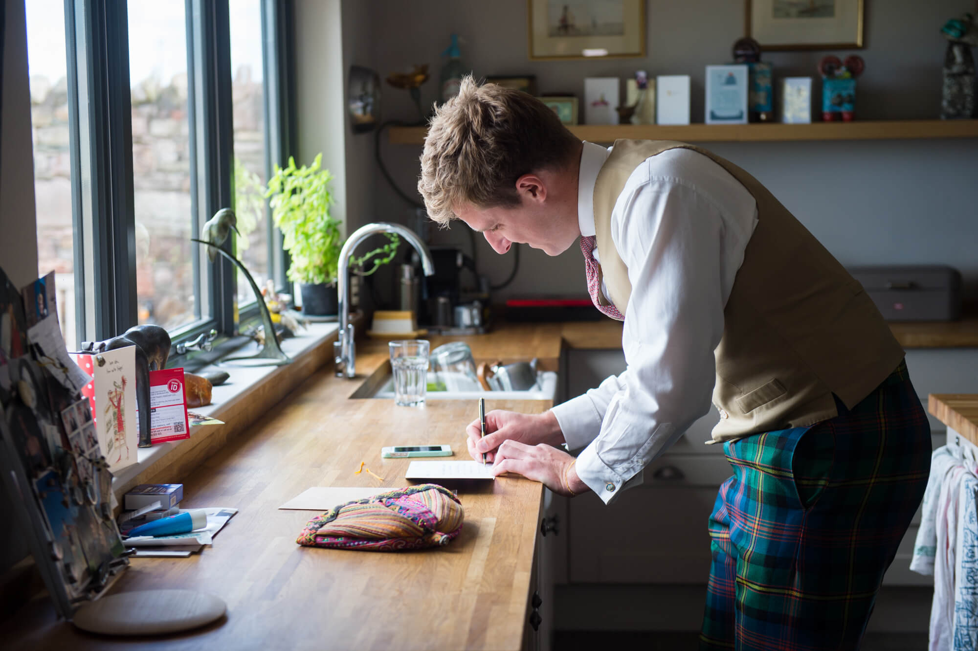 brother of the bride writing a card before the wedding wearing tartan trousers and a waistcoat